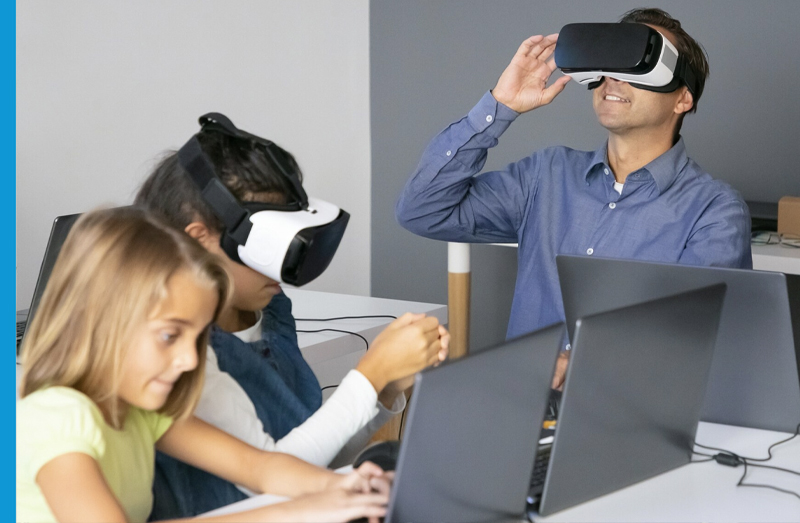 male teacher and one student have on VR headsets; another student works on laptop - photo credit: pch.vector on Freepik